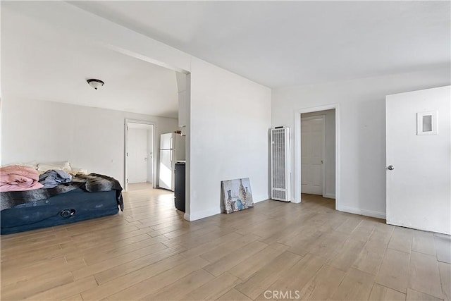 unfurnished bedroom featuring baseboards, light wood-style floors, and freestanding refrigerator