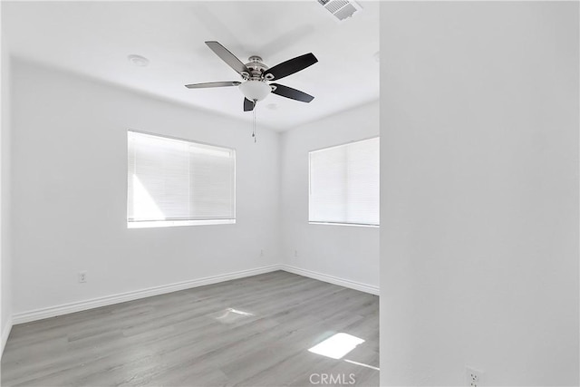 empty room with ceiling fan, visible vents, baseboards, and wood finished floors