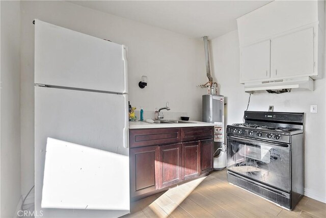 kitchen with under cabinet range hood, a sink, water heater, freestanding refrigerator, and black range with gas cooktop