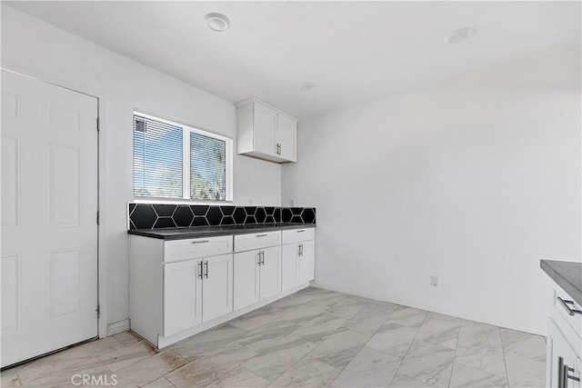 kitchen with dark countertops, marble finish floor, white cabinetry, and baseboards