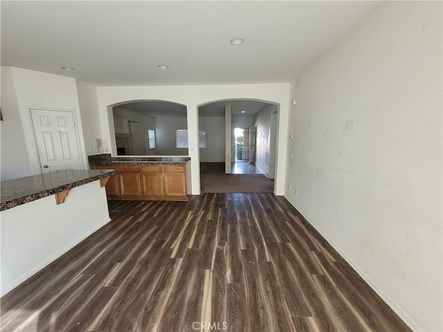 kitchen featuring a breakfast bar, dark countertops, dark wood finished floors, arched walkways, and brown cabinetry