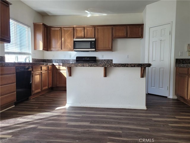 kitchen with a breakfast bar area, dark wood-style flooring, black dishwasher, stainless steel microwave, and range