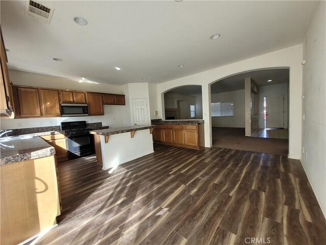 kitchen with a kitchen bar, visible vents, stainless steel microwave, dark wood-style floors, and black gas range oven