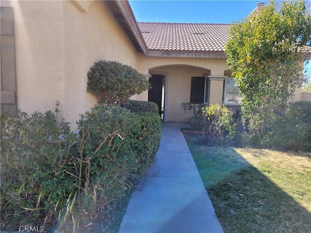 doorway to property featuring stucco siding, a yard, and a tile roof