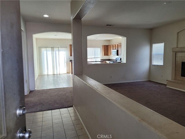 hallway with tile patterned flooring, visible vents, baseboards, carpet, and arched walkways