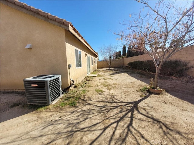 view of side of home featuring a tile roof, stucco siding, fence private yard, and central AC