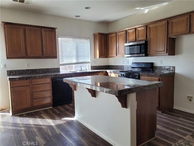 kitchen featuring dark wood finished floors, black appliances, a kitchen breakfast bar, and a center island