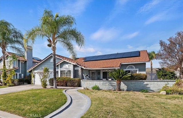 mediterranean / spanish house featuring solar panels, a tile roof, concrete driveway, a front yard, and an attached garage