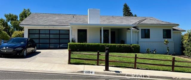 view of front of property featuring fence, driveway, an attached garage, a chimney, and a front lawn