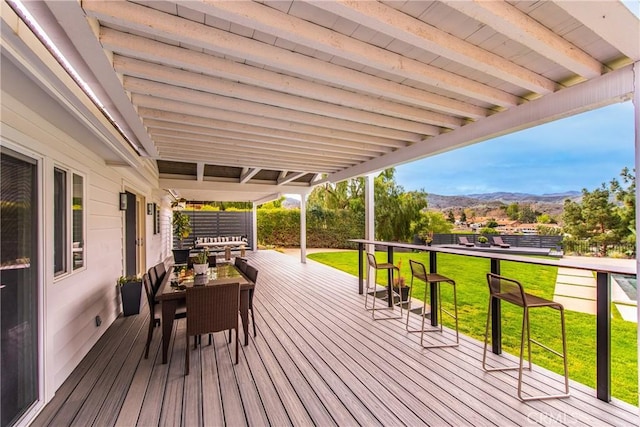 wooden terrace with outdoor dining area, a mountain view, and a lawn