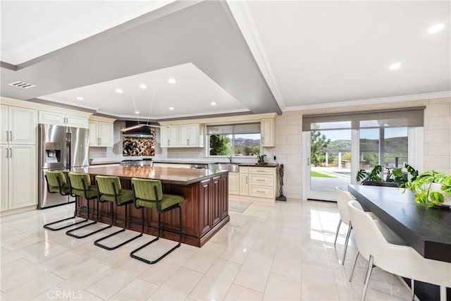 kitchen with ventilation hood, a kitchen island, a kitchen bar, crown molding, and stainless steel fridge