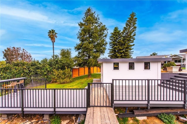 rear view of house featuring stucco siding, a yard, a wooden deck, and fence