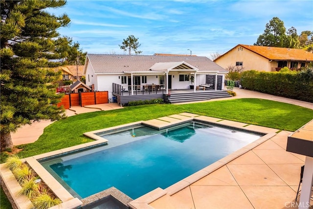 rear view of house featuring a hot tub, fence, a tile roof, a lawn, and a deck