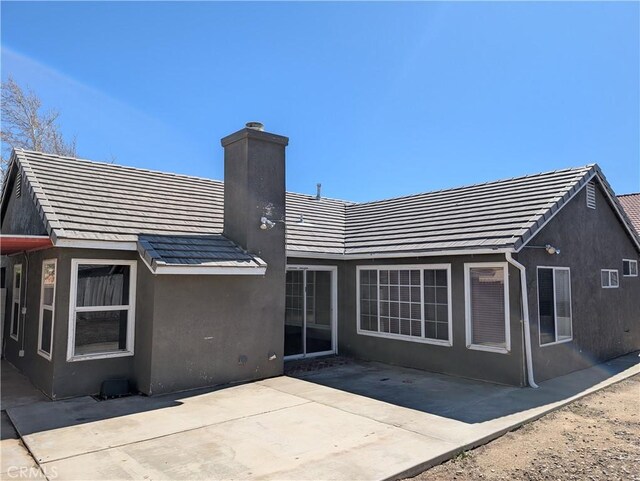 back of house featuring a patio, a tiled roof, a chimney, and stucco siding