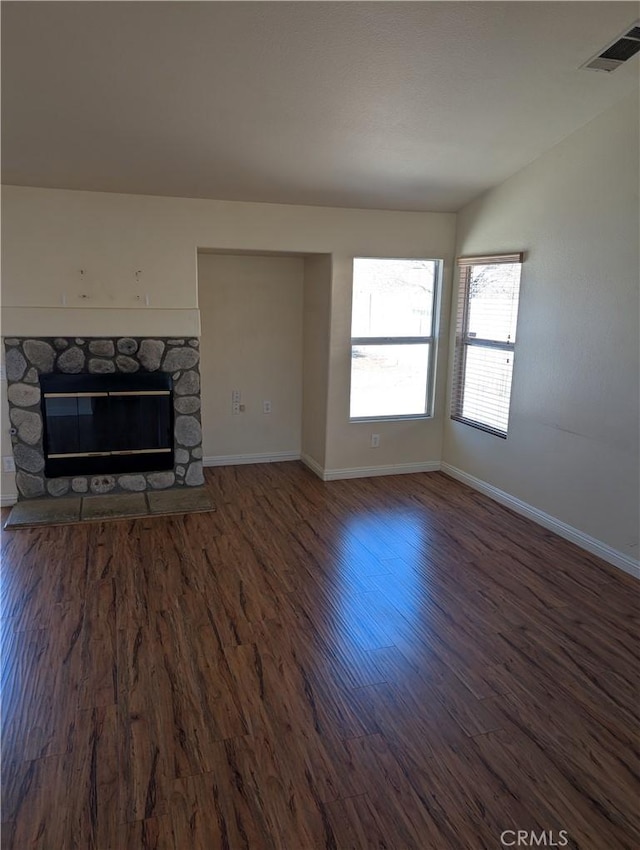 unfurnished living room with a stone fireplace, visible vents, wood finished floors, and baseboards