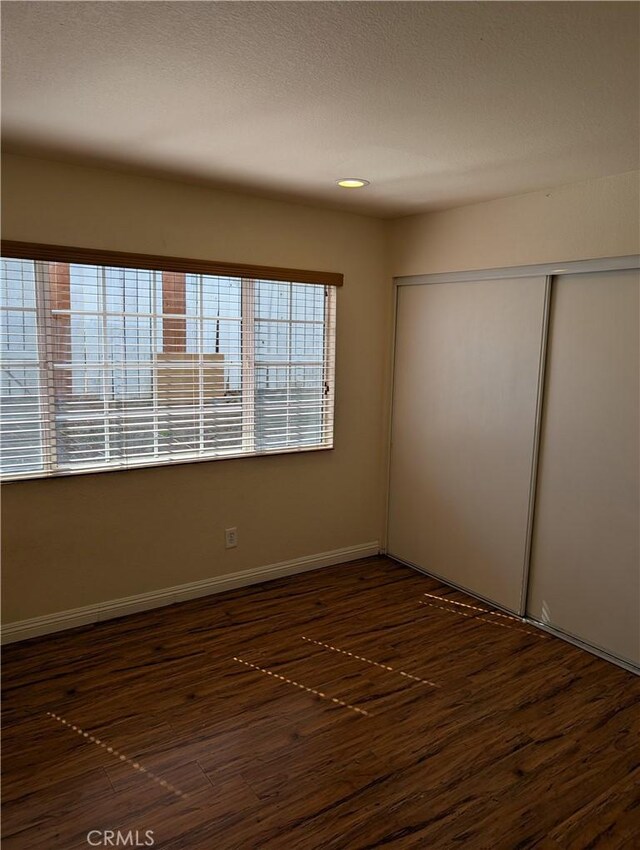 unfurnished room with dark wood finished floors, a textured ceiling, and baseboards