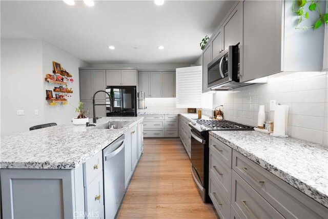 kitchen with a sink, light wood-type flooring, appliances with stainless steel finishes, and gray cabinetry