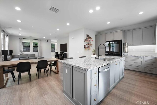 kitchen featuring visible vents, a sink, gray cabinetry, dishwasher, and open floor plan