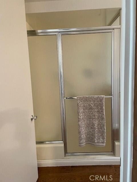 bathroom featuring wood finished floors and bath / shower combo with glass door