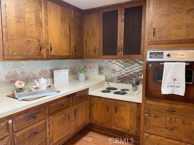 kitchen featuring brown cabinetry, wall oven, white electric stovetop, and light countertops