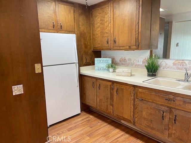 kitchen featuring light wood-type flooring, brown cabinets, a sink, freestanding refrigerator, and light countertops