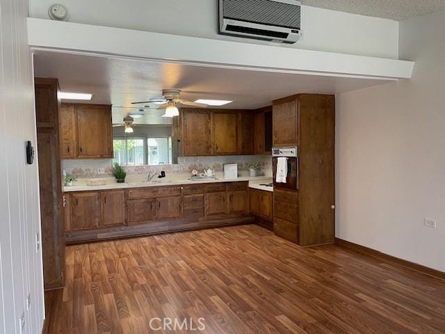 kitchen with brown cabinetry, a textured ceiling, light countertops, and wood finished floors