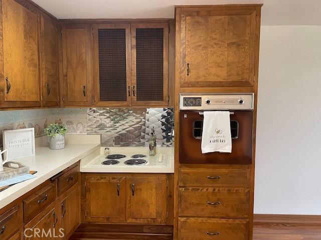 kitchen featuring brown cabinets, backsplash, white electric cooktop, wall oven, and light countertops