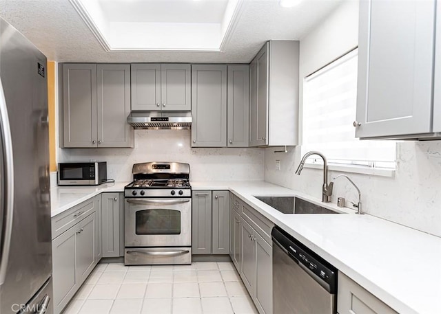 kitchen featuring gray cabinetry, under cabinet range hood, a sink, tasteful backsplash, and appliances with stainless steel finishes