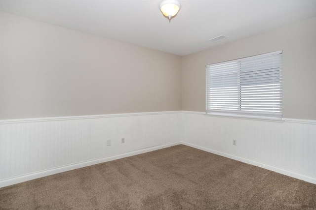 carpeted empty room featuring visible vents and a wainscoted wall