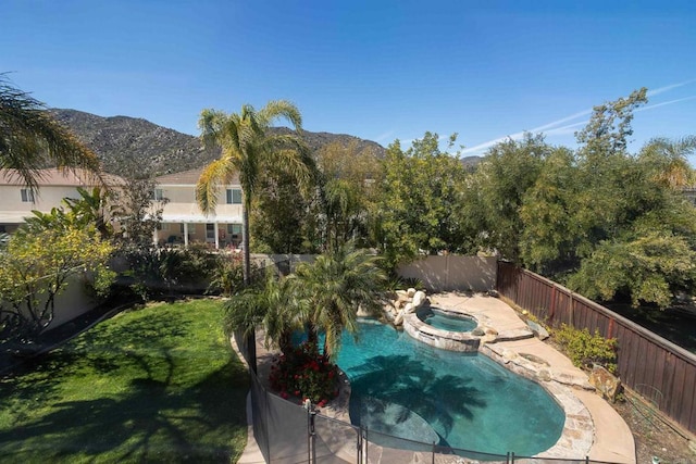 view of swimming pool featuring a mountain view, a yard, a fenced backyard, and a pool with connected hot tub