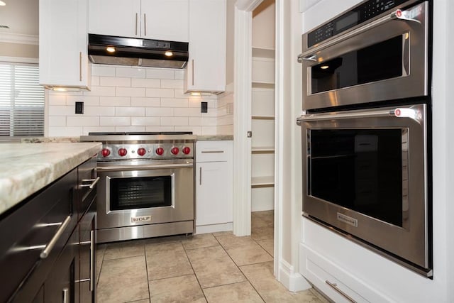 kitchen with under cabinet range hood, white cabinets, stainless steel appliances, and tasteful backsplash