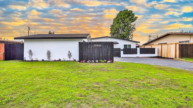 exterior space featuring fence, stucco siding, a lawn, driveway, and a gate