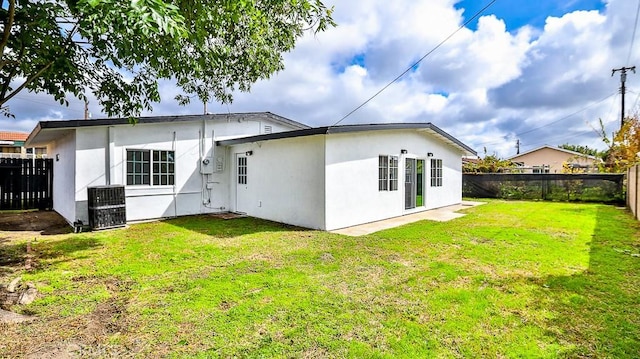 rear view of house with a yard, central AC unit, a fenced backyard, and stucco siding