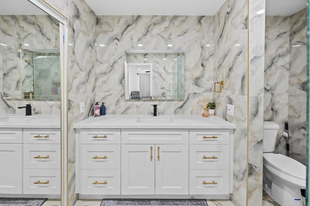 bathroom featuring toilet, tile walls, two vanities, and a sink