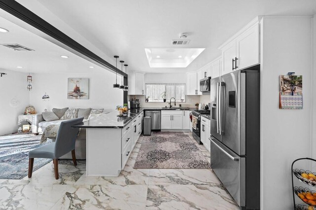 kitchen featuring visible vents, a tray ceiling, a sink, stainless steel appliances, and dark countertops