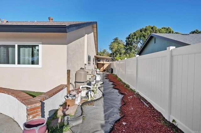 view of side of home with stucco siding, a fenced backyard, and a shingled roof