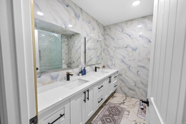 bathroom featuring a sink, stone wall, marble finish floor, and double vanity