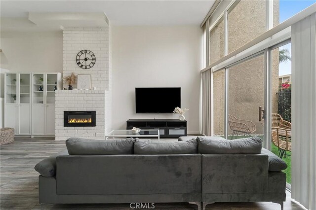 living room featuring a wall of windows, a brick fireplace, and wood finished floors