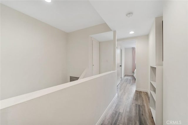 hall featuring recessed lighting, wood finished floors, baseboards, and an upstairs landing