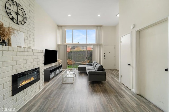 living area featuring recessed lighting, a fireplace, a towering ceiling, and wood finished floors