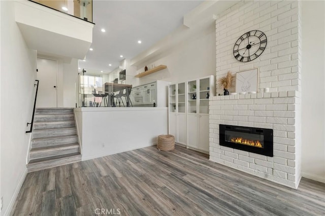 unfurnished living room with stairway, wood finished floors, baseboards, a fireplace, and recessed lighting