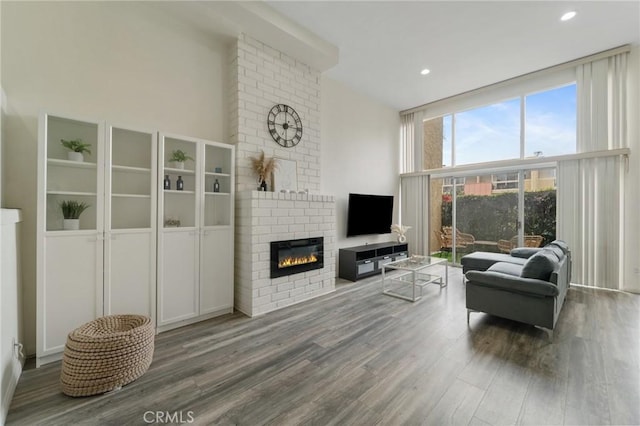 living area with high vaulted ceiling, wood finished floors, floor to ceiling windows, recessed lighting, and a fireplace