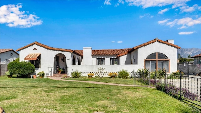 mediterranean / spanish home with a tiled roof, fence private yard, a front yard, stucco siding, and a chimney