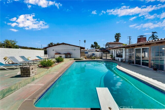 view of pool with fence, an outdoor structure, a diving board, a fenced in pool, and a patio area