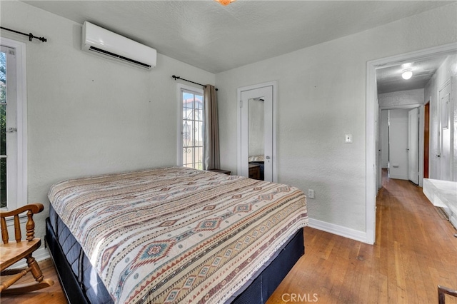 bedroom with baseboards, a wall unit AC, and wood finished floors