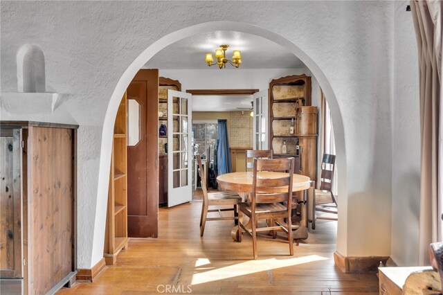 dining area with arched walkways, a textured ceiling, a textured wall, and hardwood / wood-style flooring