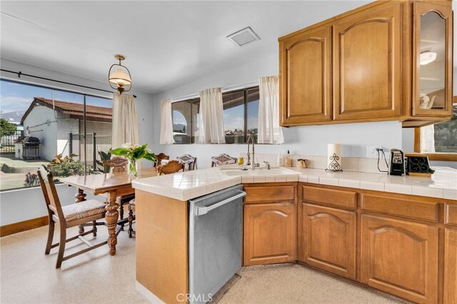 kitchen featuring glass insert cabinets, brown cabinets, a peninsula, stainless steel dishwasher, and a sink