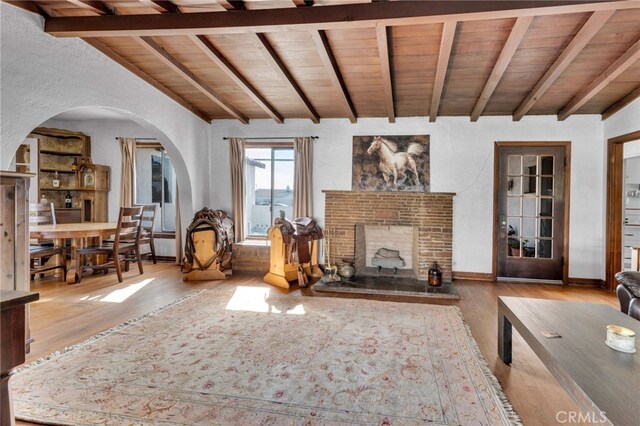 unfurnished living room with wood finished floors, lofted ceiling with beams, a fireplace, arched walkways, and wooden ceiling