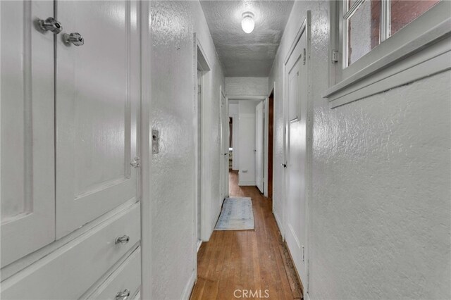 hallway featuring a textured ceiling, wood finished floors, and a textured wall