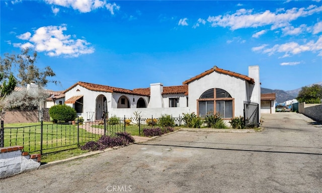 mediterranean / spanish-style house with a front lawn, a tiled roof, a fenced front yard, and stucco siding